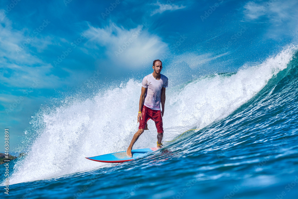 Male surfer on a blue wave at sunny day