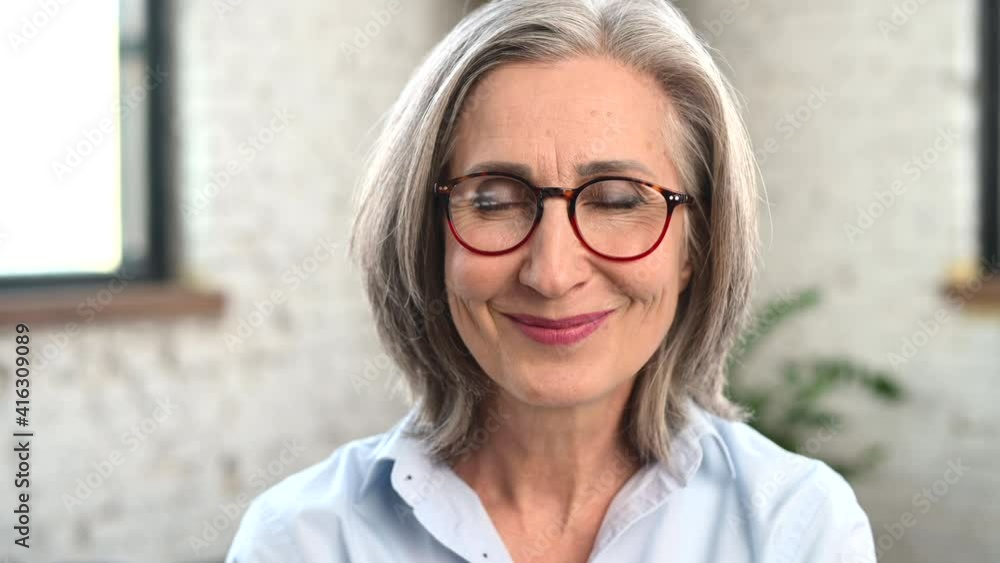 Close-up portrait of strict old senior business woman wearing smart casual shirt and stylish eyeglasses looks serious and then slimes friendly. A mature bossy lady, elderly purposeful leader Close-up portrait of strict old senior business woman wearing smart casual shirt and stylish eyeglasses looks serious and then slimes friendly. A mature bossy lady, elderly purposeful leader