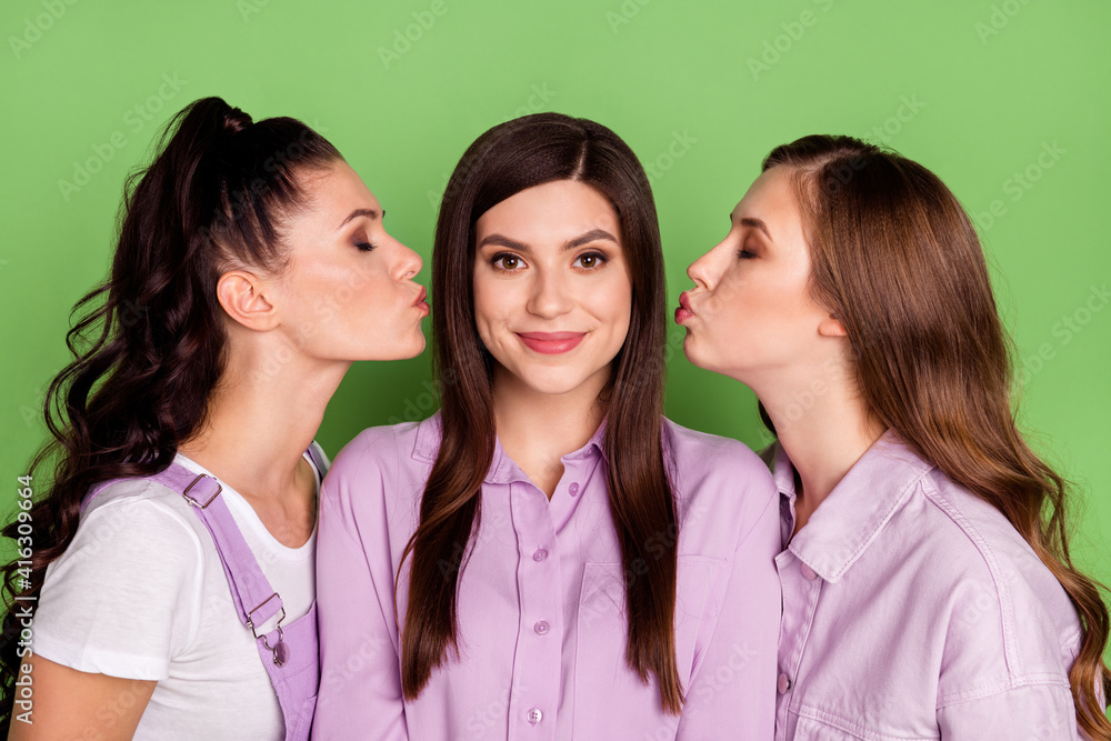 Photo of three young attractive girls happy positive smile kiss lips romantic isolated over green color background Photo of three young attractive girls happy positive smile kiss lips romantic isolated over green color background