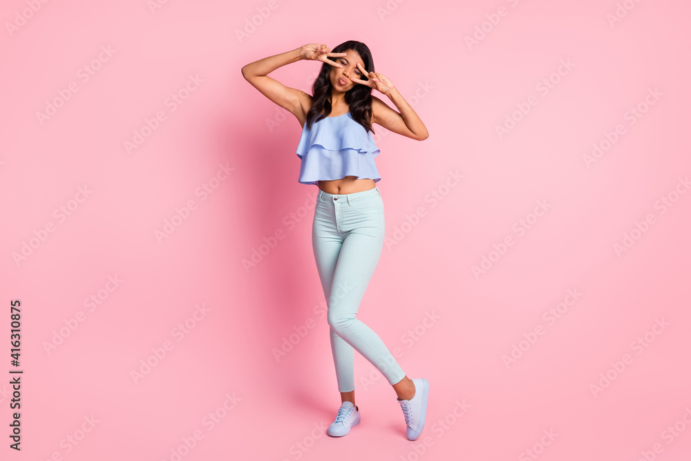 Full size photo of optimistic brunette lady show v-sign blow kiss wear blue top trousers sneakers isolated on pink color background Full size photo of optimistic brunette lady show v-sign blow kiss wear blue top trousers sneakers isolated on pink color background
