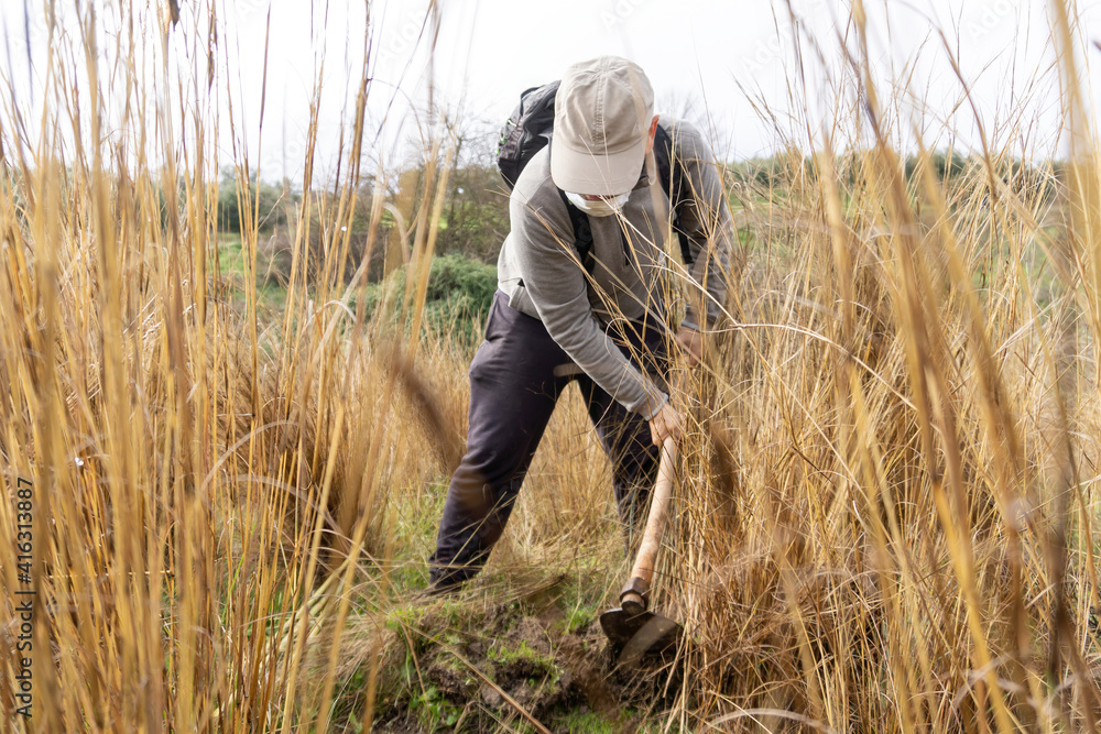 Stock photo of unrecognized man wearing face mask using shovel in the countryside helping to reforest. Selective focus. Stock photo of unrecognized man wearing face mask using shovel in the countryside helping to reforest. Selective focus.
