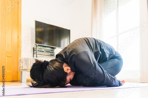 Stock photo of relaxed woman wearing sports clothes doing yoga pose in her living room.