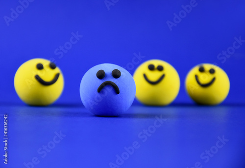 Blue sad ball and happy yellow balls stock images. Single sad blue smiley among happy yellow ones stock photo. Depressed ball on a blue background images