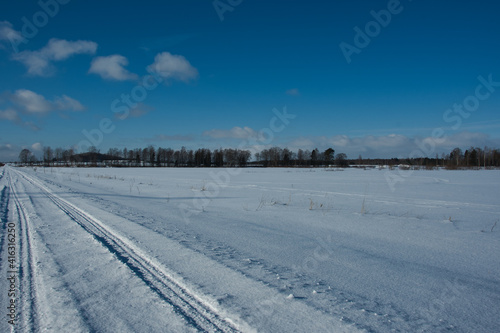 Landscape of a winter road on a completely snowy white field under a blue sky with sparse clouds on a sunny frosty day. © Alexander Korotkov