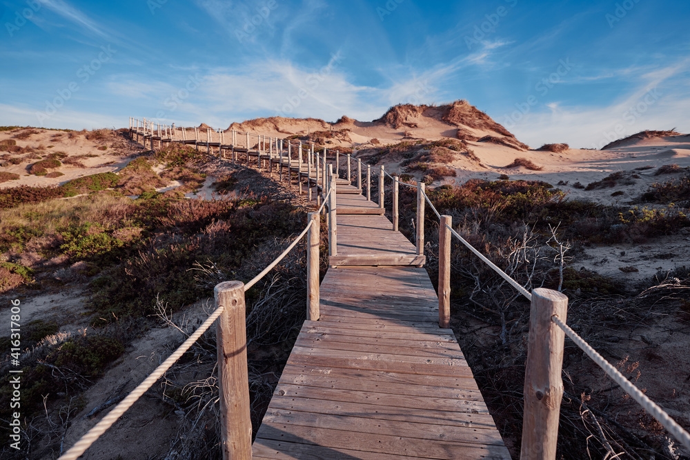 Wooden pedestrian walkway through Sintra-Cascais natural park. Wild sandy landscape, with part of Cresmina Dunes. Beautiful scenery in Portugal. Wooden pedestrian walkway through Sintra-Cascais natural park. Wild sandy landscape, with part of Cresmina Dunes. Beautiful scenery in Portugal.