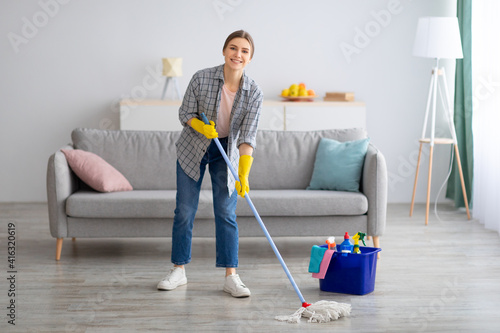 Fotografija Pretty young lady wiping floor with mop, doing house cleanup, free space