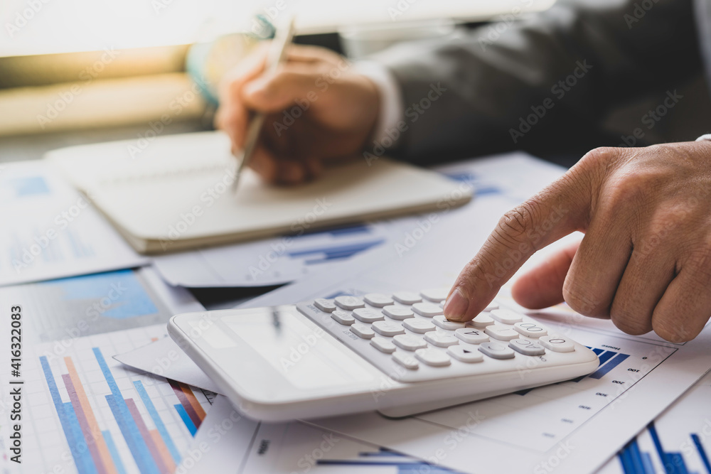 Fototapeta premium Asian male finance staff is calculating the investment results to deliver a report to his supervisor at the meeting. On the table in the office, the concept of calculating investment results