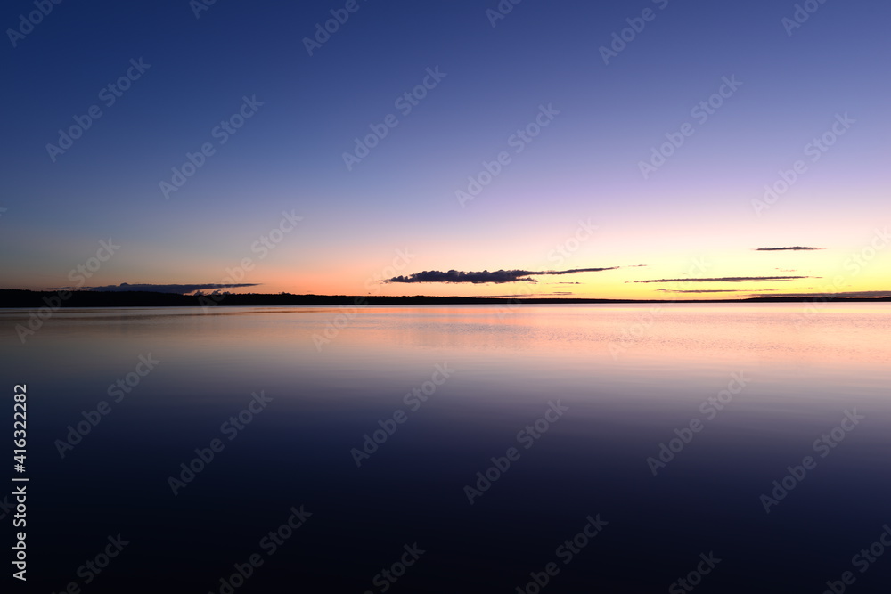 Blue sky in the orange twilight glow on horizon over calm azure water lake