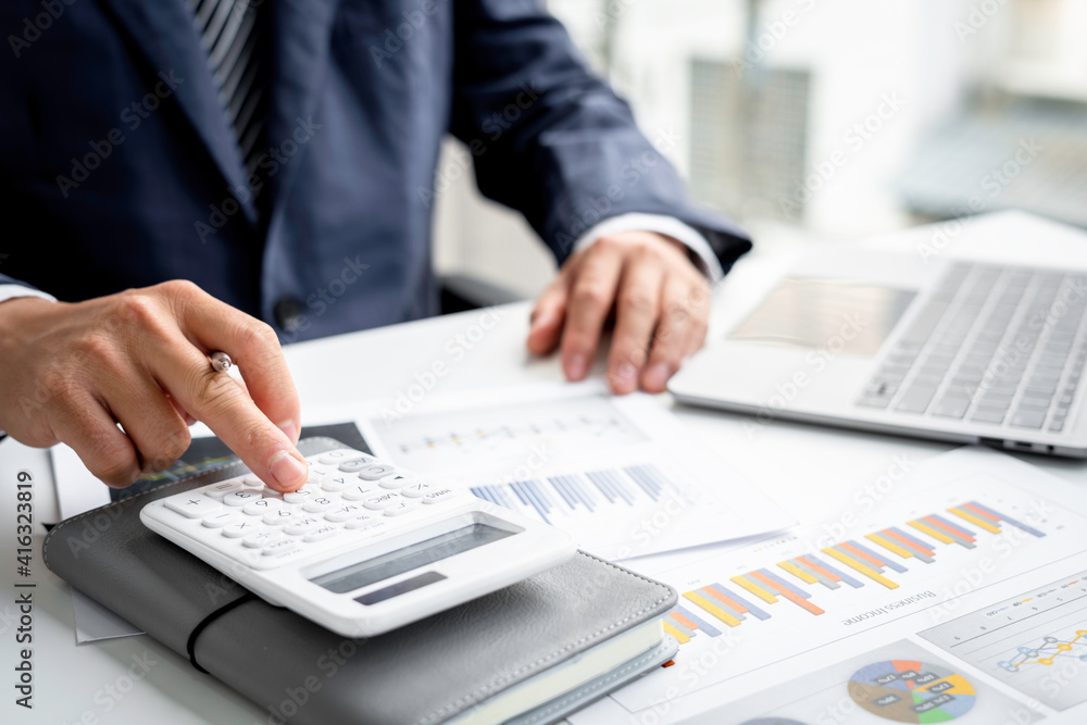A close-up of an Asian male finance man's hand pressing a calculator on a desk in an office. A close-up of an Asian male finance man's hand pressing a calculator on a desk in an office.