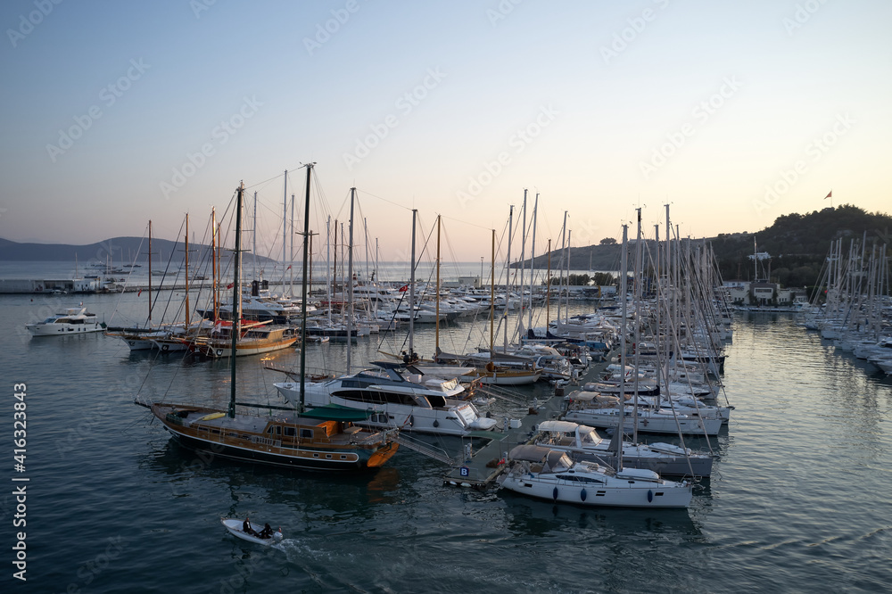 Marina in Bodrum, Turkey. Harbor with anchored boats at calm Aegean sea. Beautiful sunset sky in the background.