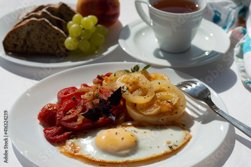 Breakfast of fried eggs and vegetables, in the background a cup of tea, a banana muffin and grapes on a plate.
