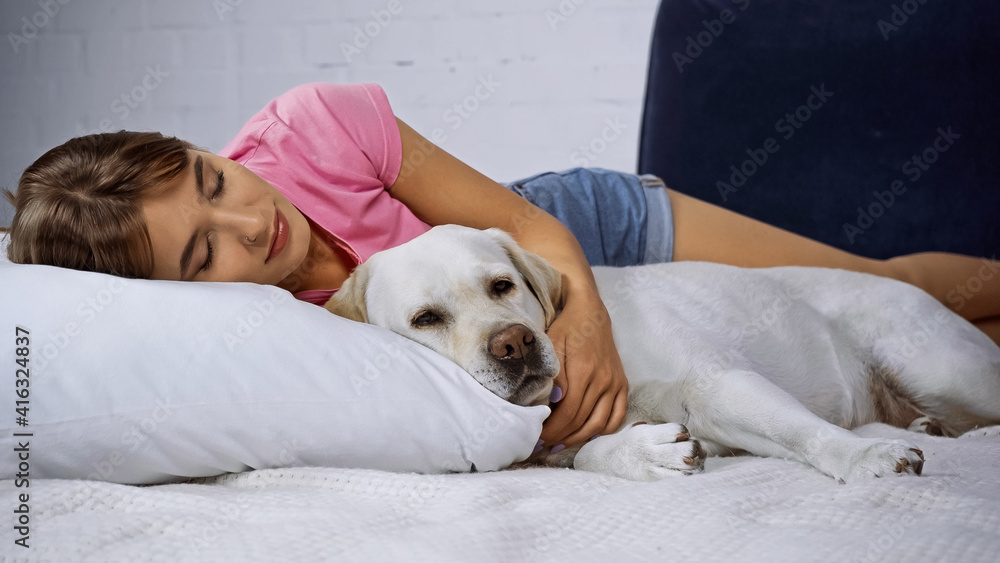 young woman with closed eyes lying with golden retriever on bed
