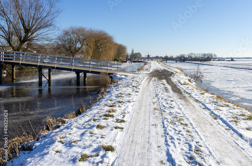 frozen and snowy Dutch landscape with clear blue sky. frozen water in canal. copy space. people in background are ice skating © Robin