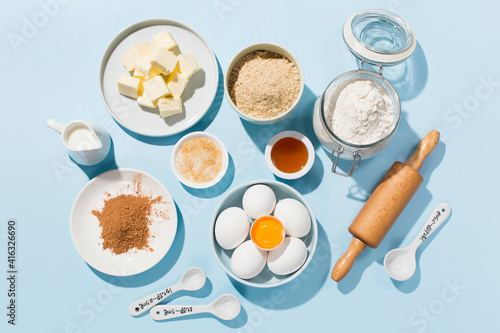 Cooking baking background with ingredients, butter, flour, eggs, spices and utensils on blue background
