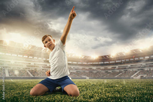 Junior football or soccer player at stadium in flashlight. Young male sportive model training. Moment of win celebrating. Concept of sport  competition  winning  action  motion  overcoming.