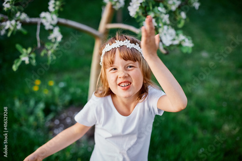 Portrait of funny kid girl 5-6 year old holding flower standing in blossom spring garden