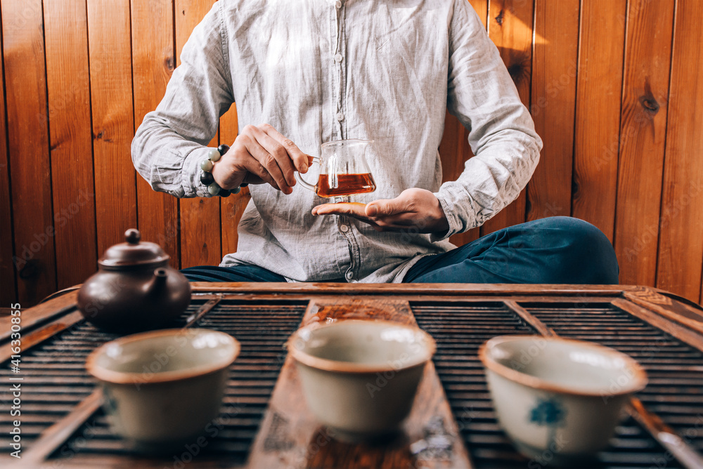 Chinese tea ceremony, a man pours tea into cups on a bamboo table, sunlight