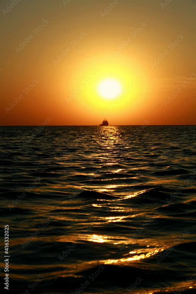 Sea sunset. On the horizon, a ship is sailing towards the sun.