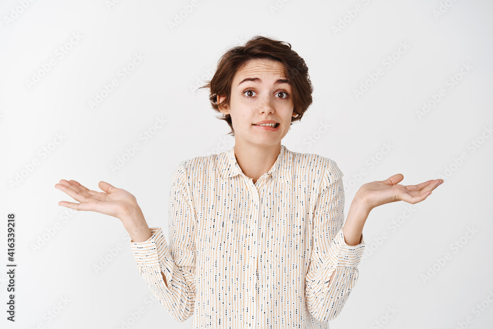 Confused silly woman know nothing, shrugging shoulders and standing with hands spread sideways, saying oops as making small mistake, white background Confused silly woman know nothing, shrugging shoulders and standing with hands spread sideways, saying oops as making small mistake, white background