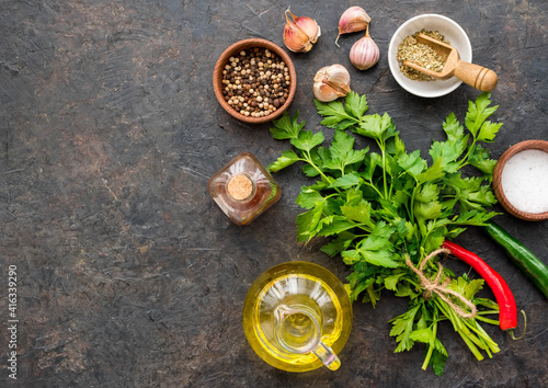 Prepared ingredients for Chimichuri, Argentinean green steak sauce with fresh parsley, garlic, olive oil and oregano on a dark concrete background. Sauce recipes.