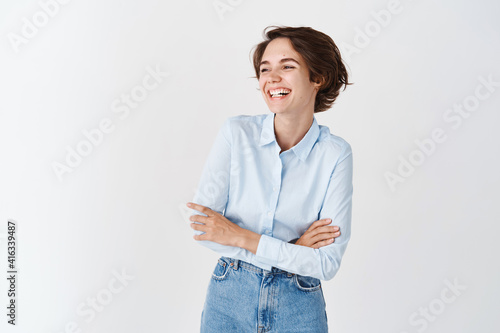 Candid young office woman in blue collar shirt, laughing and smiling happy, looking aside at empty space logo, standing on white background