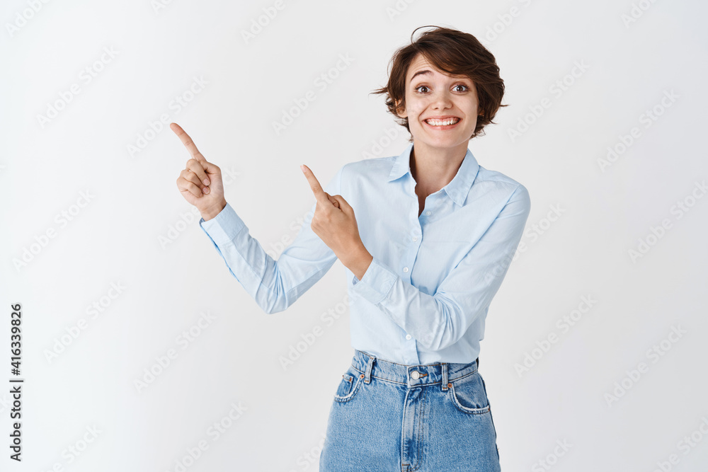 Happy caucasian woman in blue collar shirt and jeans, smiling cheerful and pointing at upper left corner logo, standing on white background Happy caucasian woman in blue collar shirt and jeans, smiling cheerful and pointing at upper left corner logo, standing on white background