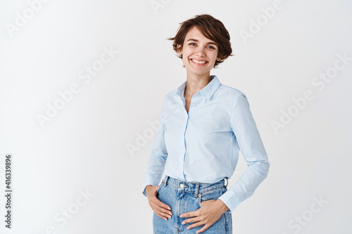Papier peint Young working woman in office clothing, smiling and looking at camera, standing on white background