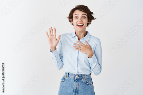 Cheerful young natural woman raising hand up, introduce herself or willing to participate, self-promoting on white background photo