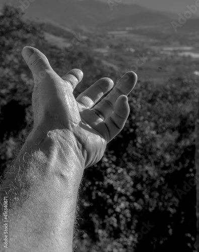 Dramatic high contrast black and white image of a hand reaching out in the Caribbean mountains with sunlight passing through fingers.