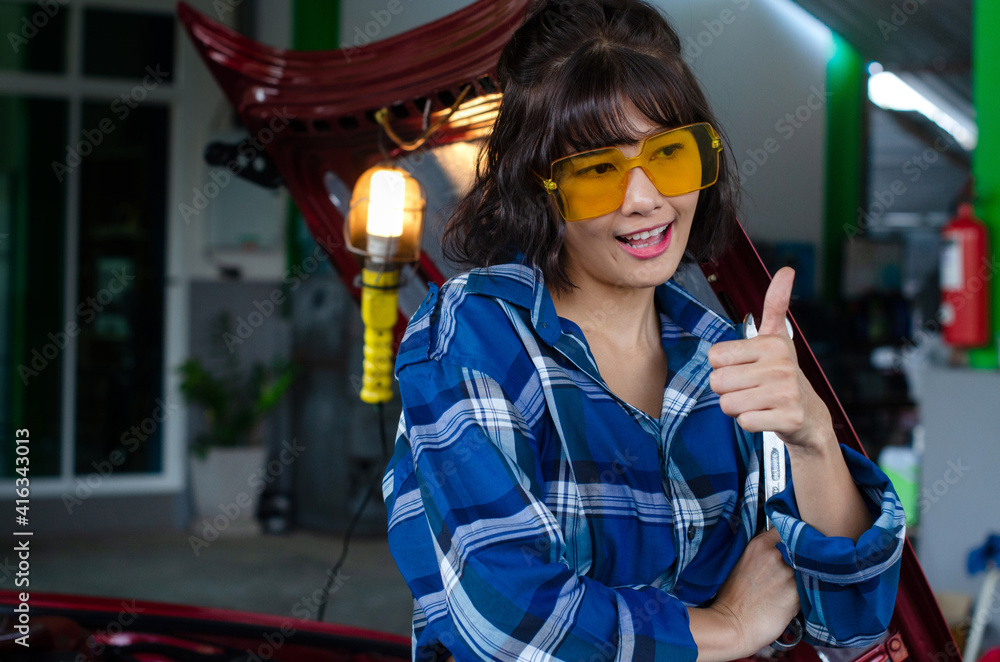 Asian female mechanic working at the repair garage, showing thumbs up gesture, car repair and maintenance, woman worker concept