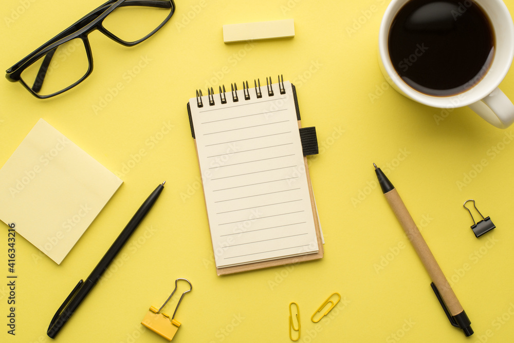 Photo above of notebook pen cup of coffee glasses and paperclips isolated on the yellow background Photo above of notebook pen cup of coffee glasses and paperclips isolated on the yellow background