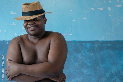 Portrait half body with no shirt of forty five years old friendly African man wearing hat, against blue wall background,  looking at camera © chomplearn_2001