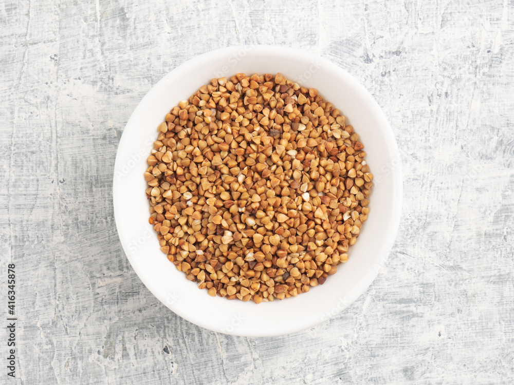 Buckwheat in a ceramic white cup on a white concrete background Buckwheat in a ceramic white cup on a white concrete background