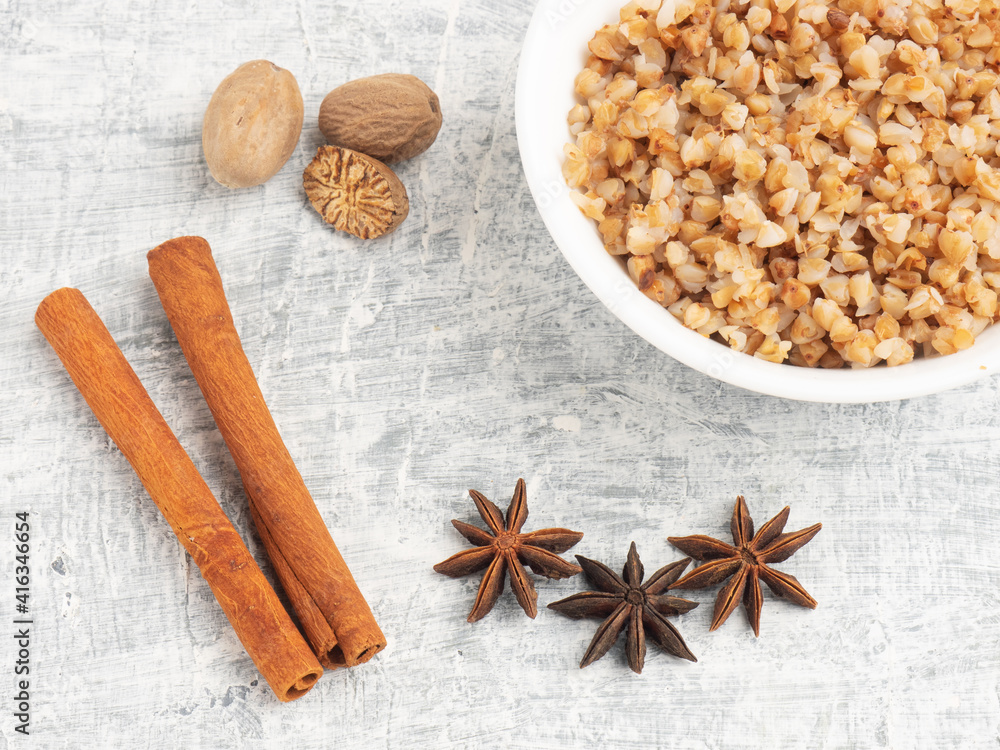 Buckwheat in ceramic bowl, nutmeg, cinnamon, star anise on white concrete background Buckwheat in ceramic bowl, nutmeg, cinnamon, star anise on white concrete background
