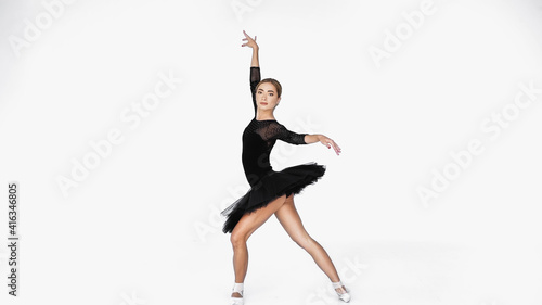 elegant ballerina in tutu skirt and pointe shoes dancing on white background