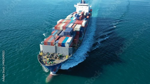 Aerial drone rotational video of Container cargo Ship carrying load in truck-size colourful containers in deep blue open ocean sea 