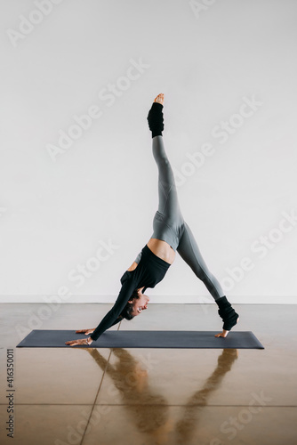 Fototapeta Naklejka Na Ścianę i Meble -  Fit young woman coach practices individual hatha yoga on a mat in a white background. Female instructor In Sport Clothes Performing Exercise.One Legged Downward Facing Dog Pose