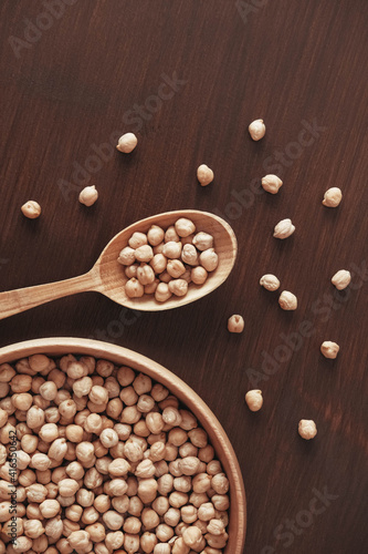 Dry chickpeas in a wooden plate and spoon on a brown wooden background. Top view. Copy, empty space for text