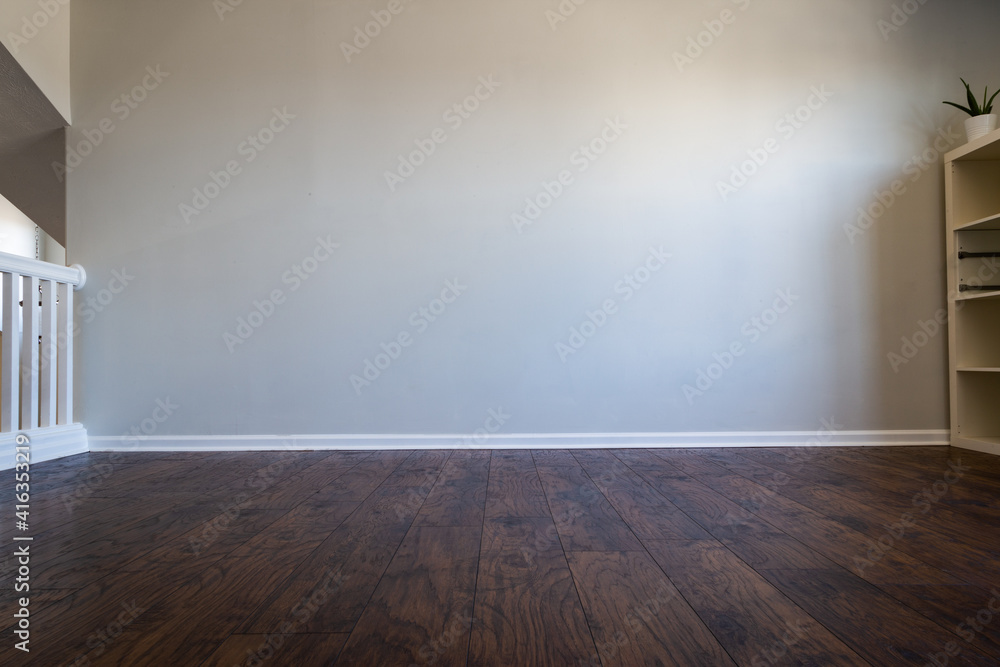 Empty room interior with laminated wood floor and gray wall. Bookshelf visible on the right side. Stair railing visible on the left side. Can be used as a backdrop for virtual furniture or decor. Empty room interior with laminated wood floor and gray wall. Bookshelf visible on the right side. Stair railing visible on the left side. Can be used as a backdrop for virtual furniture or decor.