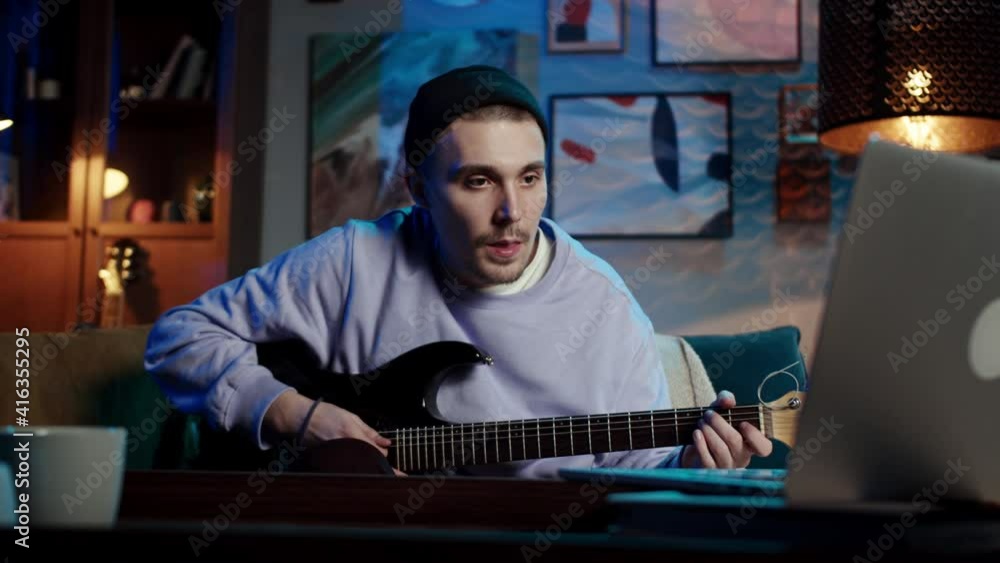young man with guitar playing songs in the room at home. Online guitar lessons concept. Male guitarist practicing chord grips. Remote learning during coronavirus lockdown young man with guitar playing songs in the room at home. Online guitar lessons concept. Male guitarist practicing chord grips. Remote learning during coronavirus lockdown
