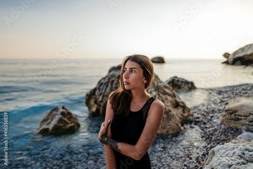 Girl in black dress posing at sunset on the rock at sea