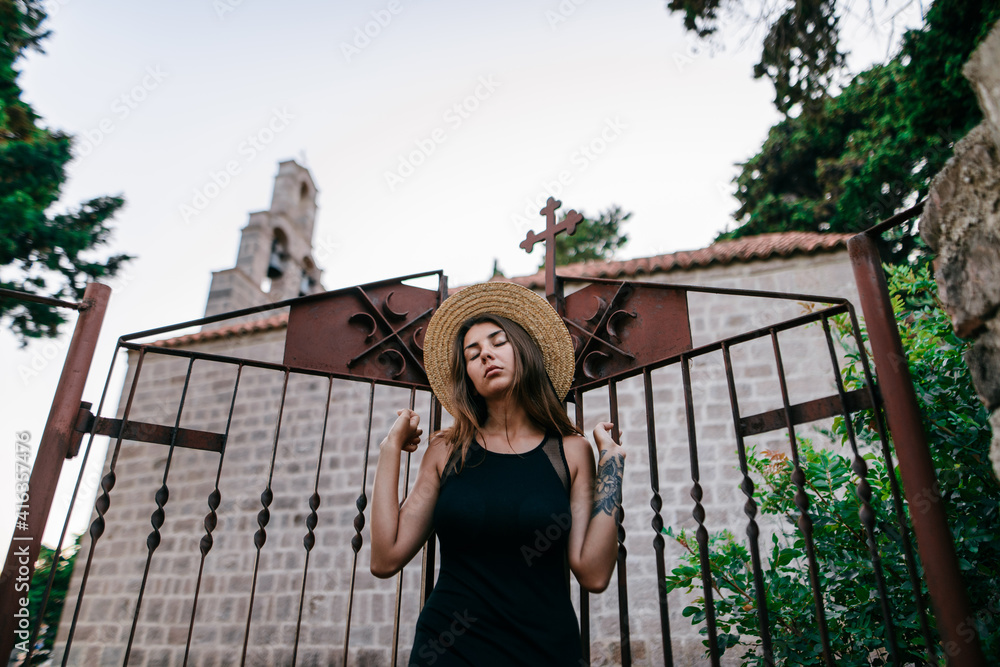 Girl in black dress in hat posing at church gate 