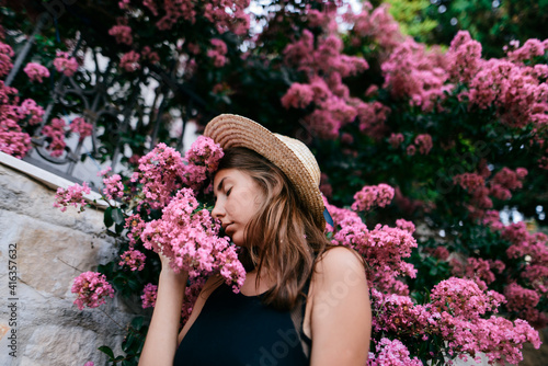Brunette girl with long hair in hat surrounded with pink flowers 