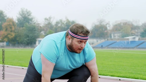 Obese charismatic man in the stadium get ready to start running he is at starting line preparing for a hard marathon photo