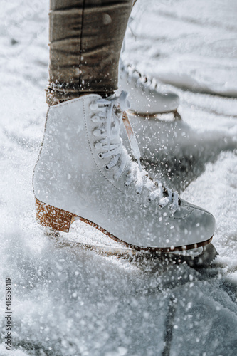 Young woman ice skating outdoors on a pond on a freezing winter day. Detail of skate shoes.