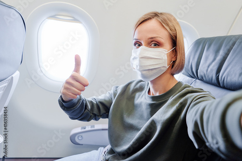 Young woman wearing face mask is traveling on airplane. New normal travel covid-19 pandemic concept.