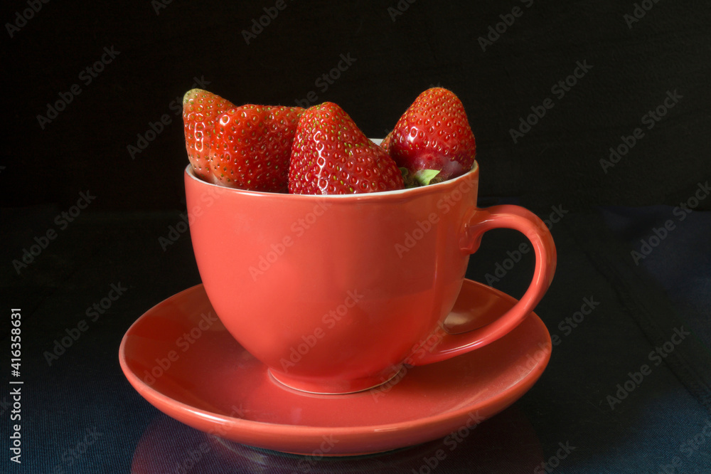 Strawberries in cup on black background and table with reflectio Strawberries in cup on black background and table with reflectio
