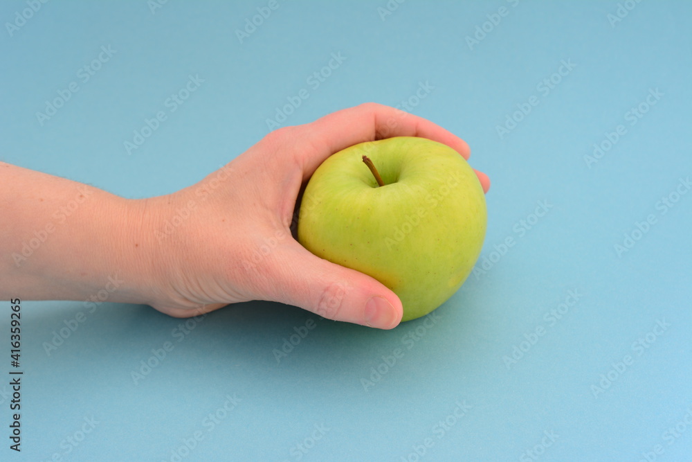 woman's hand holding green apple on the blue background woman's hand holding green apple on the blue background