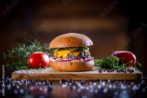 Craft beef burger with cheddar, bacon, pickles, purple onion and sauce on wooden background