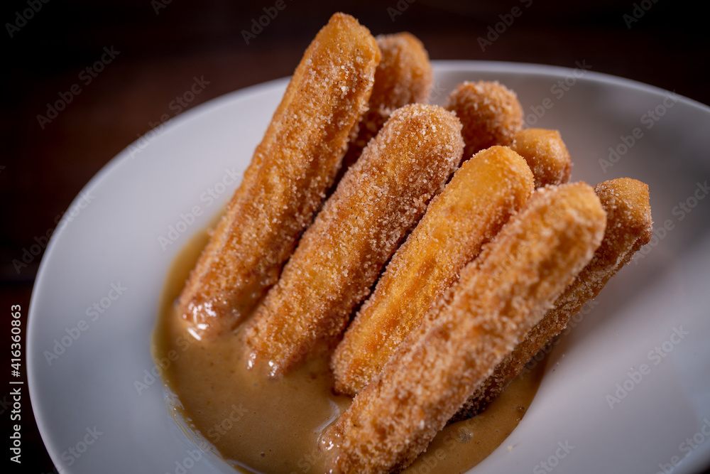 Churros sticks with caramel in a wooden background Churros sticks with caramel in a wooden background
